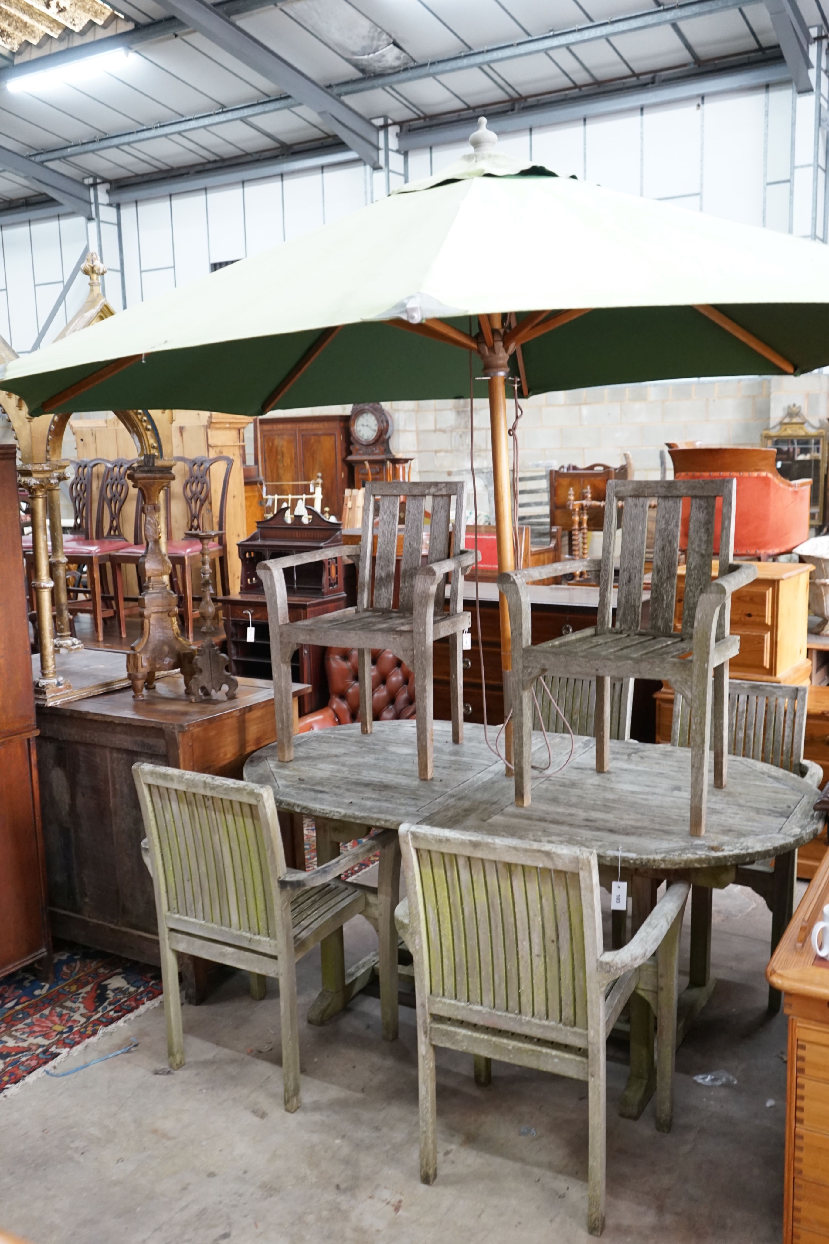 An oval weathered teak extending garden table, length 180cm, depth 100cm, height 76cm with six elbow chairs (4+2) and green canvas crank parasol